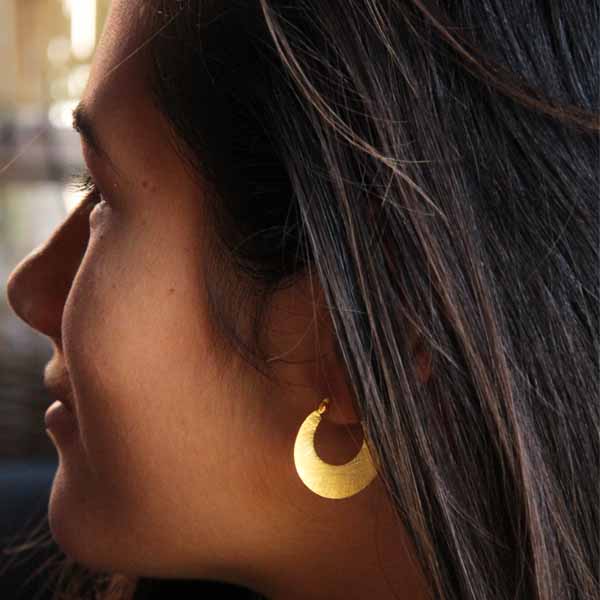 Jeune femme portant des boucles d'oreilles créoles en argent brossé dorées à l'or fin Jeune femme portant des boucles d'oreilles créoles en argent brossé dorées à l'or fin